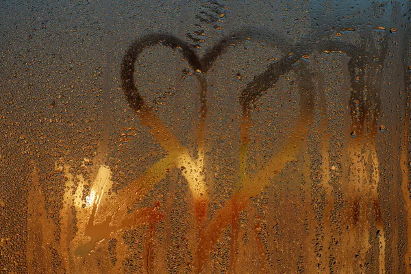 Love heart with arrow on a wet window. Closeup on foggy glass background