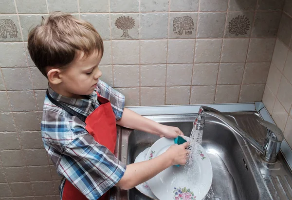 European boy washes dishes at home