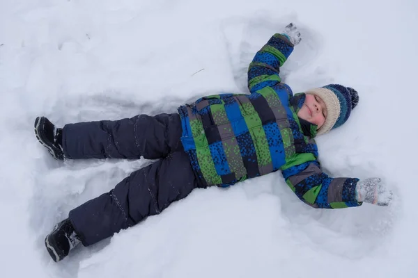 Pojke liggande i snön och vifta med armar och ben — Stockfoto