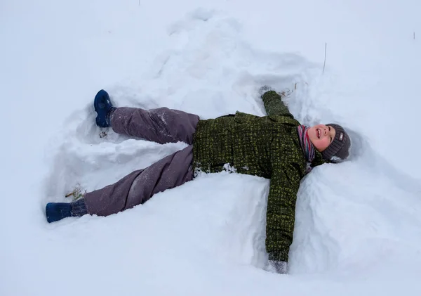 Niño acostado en la nieve y agitando brazos y piernas —  Fotos de Stock