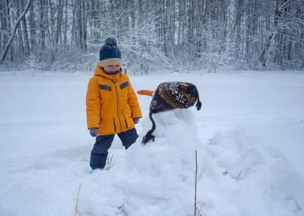 Lindo chico europeo y muñeco de nieve en el bosque —  Fotos de Stock