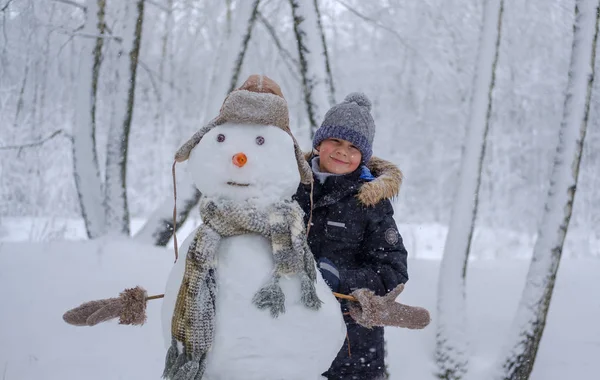 Europeiska pojke och snögubbe i en snöig skog — Stockfoto