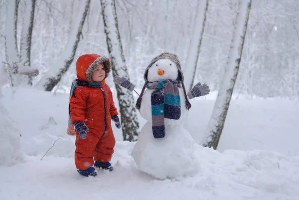 Europeiska pojke och snögubbe i en snöig skog — Stockfoto