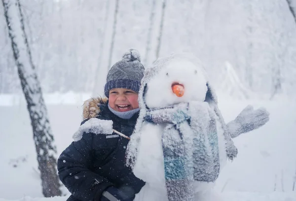 Niño europeo y el muñeco de nieve en un bosque nevado —  Fotos de Stock