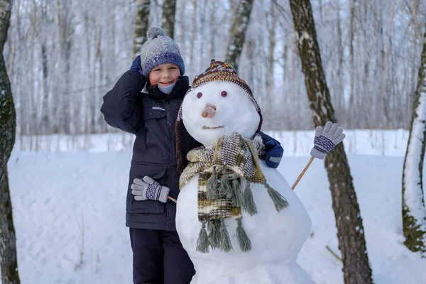 Europejskiego chłopiec i bałwan w śnieżnym lesie — Zdjęcie stockowe