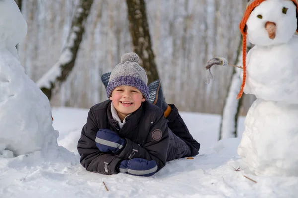 Europeiska pojke och snögubbe i en snöig skog — Stockfoto