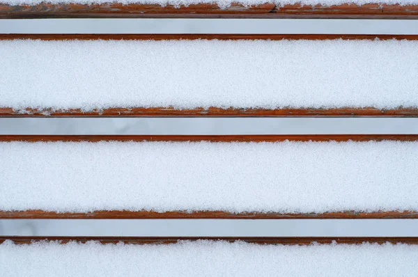 Lo sfondo naturale. panchina innevata in legno nel Parco. tavole di legno sotto uno strato di neve — Foto Stock