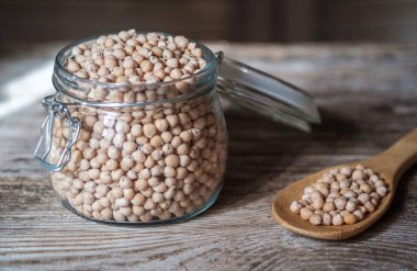 Eski bir tahtanın üzerinde cam bir kavanozda çiğ nohut. Sağlıklı vejetaryen ürünü