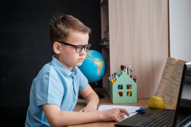 Sevimli bir çocuk evde bilgisayar ekranının önündeki masada online eğitim kursu alıyor. Covid-19 karantina döneminde okulda mesafe öğrenimi