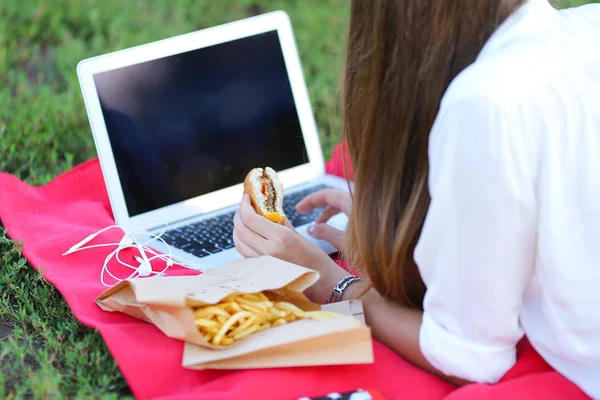 Junges Mädchen über die Natur des Fastfood-Essens und die Arbeit am Laptop — Stockfoto