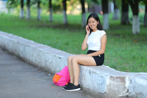 Νεαρό κορίτσι να κάθεται και να μιλάει στο τηλέφωνο στο πάρκο — Φωτογραφία Αρχείου