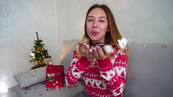 Muchacha joven retrato sonrisa a la cámara, mirada soplar Confetti árbol de Navidad Bokeh Navidad luces año nuevo Confetti — Vídeos de Stock