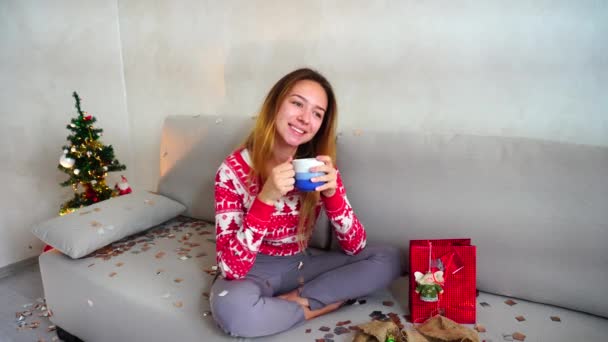 Junges Mädchen Porträt Lächeln in die Kamera, Blick trinken Tee Kaffee Weihnachtsbaum Bokeh Weihnachtsbeleuchtung Neujahr Konfetti — Stockvideo