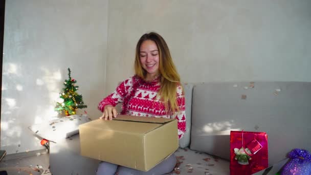 Paquete de entrega a la joven sonrisa retrato caja abierta Compras en línea en árbol de Navidad Bokeh Nochebuena luces Año Nuevo Confetti fondo en casa — Vídeos de Stock