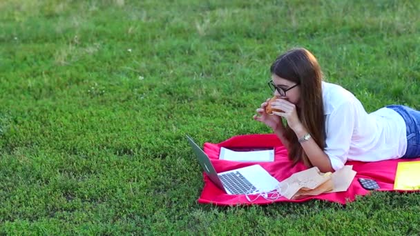 Trabajo femenino tumbado en gafas en el parque y merienda de comida — Vídeo de stock
