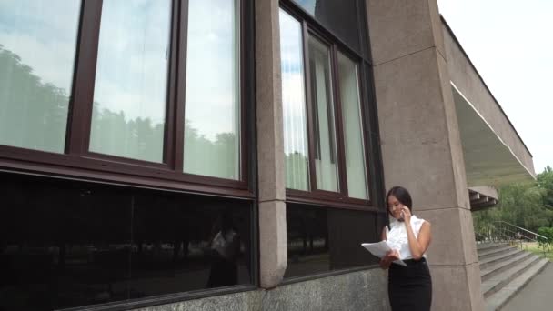 Joven hermosa mujer de negocios mujer mujer retrato hablar por teléfono mantenga documentos caminar en segundo plano edificio de oficinas al aire libre — Vídeos de Stock