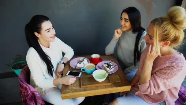 Три красивые улыбки женщины в кафе, говорить, рассказывать секреты, есть, пить кофе . — стоковое видео