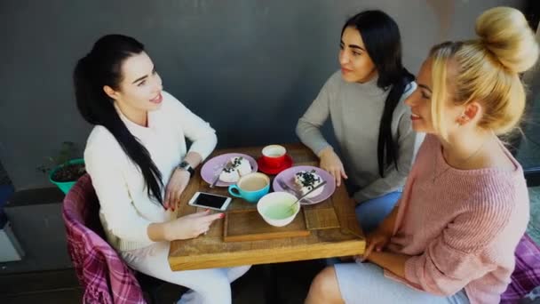 Tre belle donne sorridono nel caffè, parlare, raccontare segreti, mangiare, bere caffè . — Video Stock