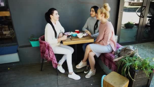 Három gyönyörű női mosoly Cafe, beszélni, elmondja a titkokat, enni, inni kávé. — Stock videók