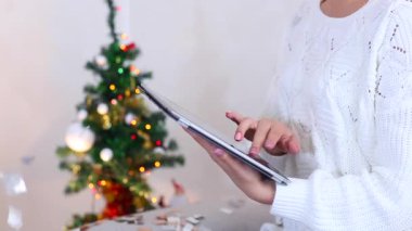Young Girl Uses Hand Hold Press Tablet on Bokeh Xmas Eve Lights New Year Tree Confetti Christmas