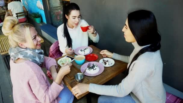 Tres hermosas mujeres sonríen en Café, Hablar, Contar Secretos, Comer, Beber Café . — Vídeos de Stock