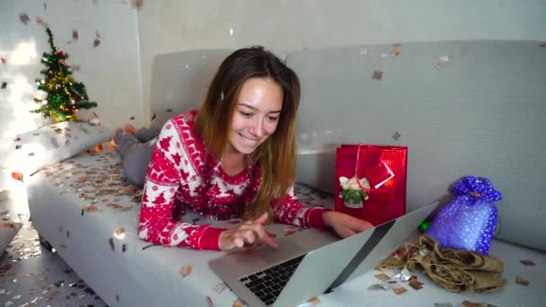 Портрет молодої дівчини Посмішка Використовуйте ноутбук для онлайн-покупки з кредитною дебетовою карткою Різдвяна ялинка Боке Різдвяні вогні Новий рік Конфетті Фон вдома — стокове відео