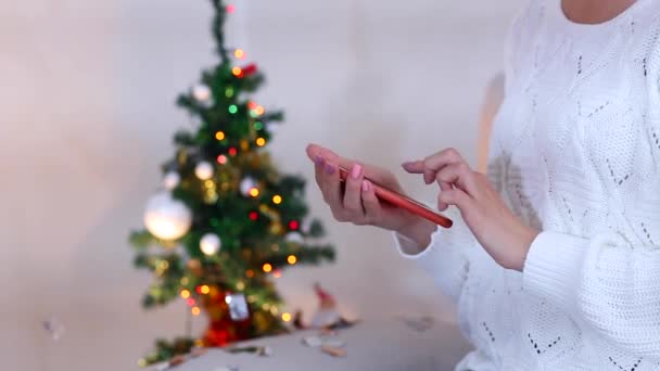 Chica joven utiliza prensas de mano pantalla del teléfono táctil en Bokeh Nochebuena luces árbol de año nuevo Confetti Navidad — Vídeos de Stock