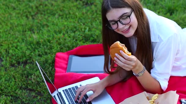 手の女はキーボードを押し、緑の草の上にファーストフードを食べる — ストック動画