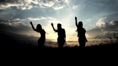Üç genç ince kız pratik Yoga açık havada günbatımı karşı siluetleri.