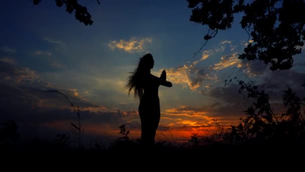 Silhouet tegen kleurrijke zonsondergang een sierlijke meisje het beoefenen van Yoga buiten. — Stockvideo