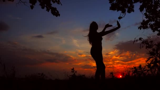 Silhouette contro il tramonto arancione rosso di una giovane ragazza graziosa che pratica yoga all'aperto . — Video Stock