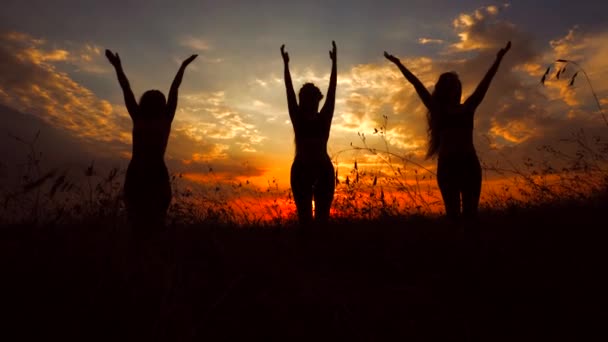 Silhouetten vor rotem Sonnenuntergang von drei jungen schlanken Mädchen, die im Freien Yoga praktizieren. — Stockvideo