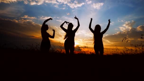 Silhouette contro il tramonto colorato di tre giovani ragazze snelle che praticano yoga all'aperto . — Video Stock
