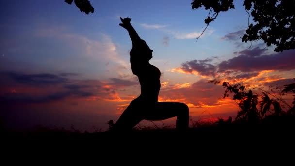 Sylwetka przeciwko kolorowy zachód słońca z jednego Młoda zgrabna dziewczyna praktykowania jogi na świeżym powietrzu. — Wideo stockowe