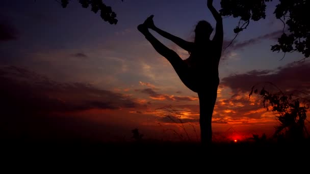 Silueta contra el colorido atardecer de una joven elegante practicando yoga al aire libre . — Vídeos de Stock