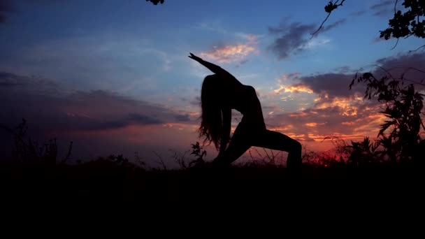 Silhouet tegen felle kleur zonsondergang een sierlijke meisje het beoefenen van Yoga buiten. — Stockvideo