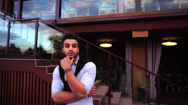 Portré fiatal gondolkodás Arab üzletember keresi a kamera, és mosolyogva a háttér európai üzleti étterem lépcsők — Stock videók