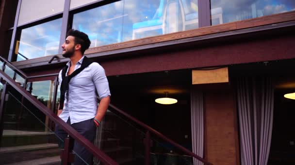 Arabic Student Young Businessman Smiles and Adjusts Sweater on Shoulders, Enjoying Life, Standing on Stairs Restaurant. — Stock video