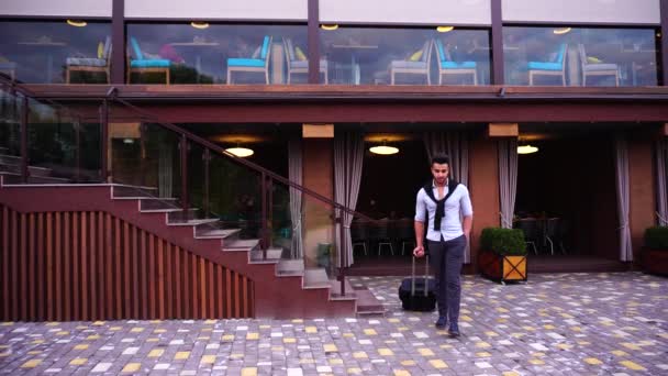 Młody Arab biznesmen go z dłoni walizkę, na tle restauracja, trzymając rękę w kieszeni i patrząc wokół. — Wideo stockowe