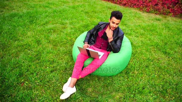 Bonito árabe jovem empresário senta-se com laptop na cadeira, olha para a tela e fora, arranhões barba e sorrindo, trabalhando on-line . — Vídeo de Stock