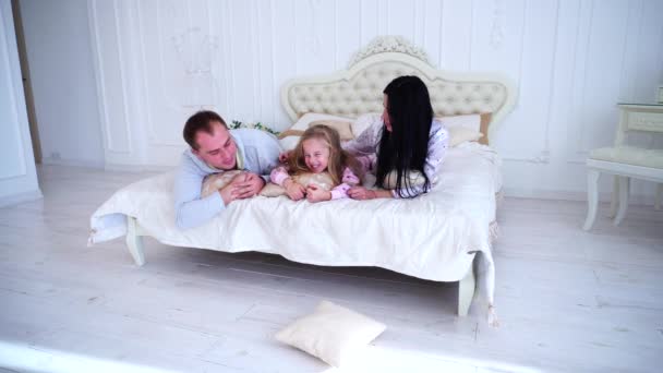 Жена, муж и дочь обнимаются и улыбаются портрет семьи в постели — стоковое видео