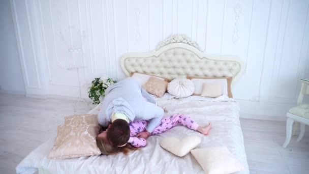 Папа щекочет дочь, играет с девушкой в постели дома — стоковое видео