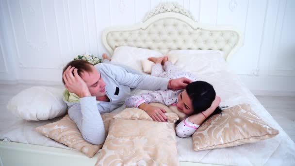 Муж обнимает жену в постели рано утром в белой комнате — стоковое видео