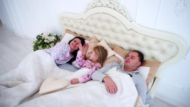 Jonge familie met dochter liggen in witte kamer op Bed, meisje wakker — Stockvideo