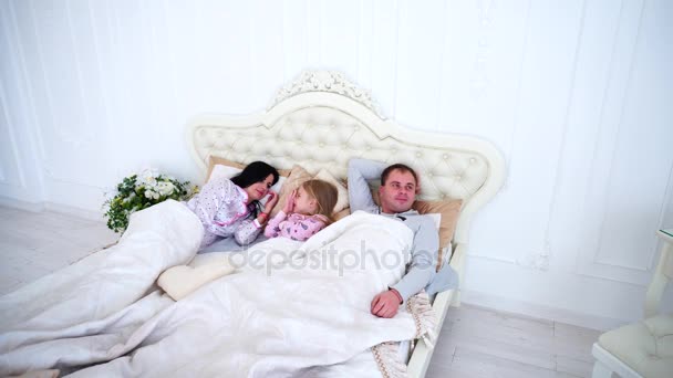 Happy Family liggend in een witte Bed en slaap. Moeder, vader en dochter wakker samen — Stockvideo