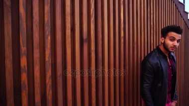 Karizmatik genç Arap adam poz ve gülümsüyor ve kamera, merdiven Restoran açık havada arka plan üzerinde gösterir jestleri bakarak.