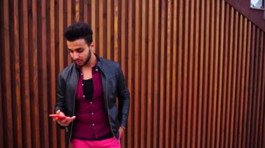 Poslu genç Müslüman adam telefon tutar ve okuma mesajı ve üzgün, arka plan açık havada merdivenin üzerinde duruyor.