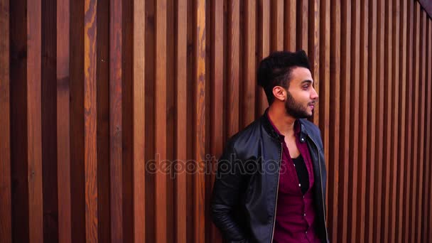 Beautiful Young Adult Muslim Man Looks at Sides and in Camera, Smiles and Stands Near Wooden Wall Near Restaurant in Open Air. — Stock Video