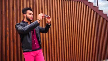 Yakışıklı genç Arapça adam kamera için poz ve ceket veya saç, düzeltiyor gülümsüyor ve merdiven arka plan açık havada etrafına bakıyor.