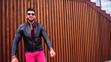 Yakışıklı genç Arapça adam kamera için poz ve ceket veya saç, düzeltiyor gülümsüyor ve merdiven arka plan açık havada etrafına bakıyor.